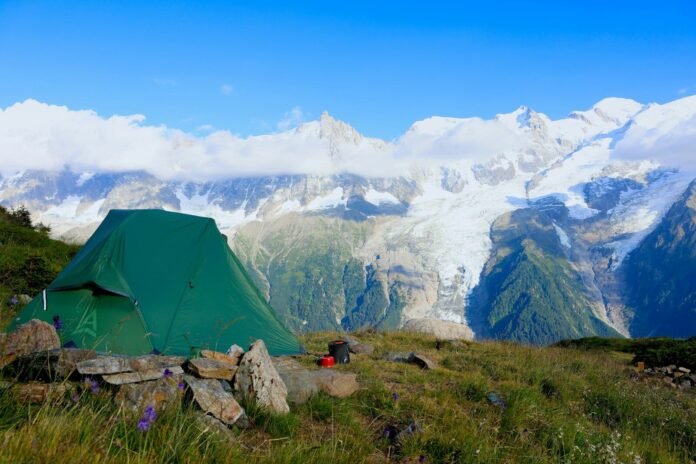 Photo by Damien Reviron A green tent set up on a grassy mountain slope.