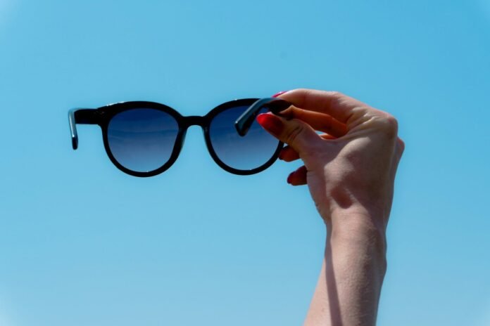 Photo by Zulfugar Karimov Hand holding sunglasses against a clear blue sky