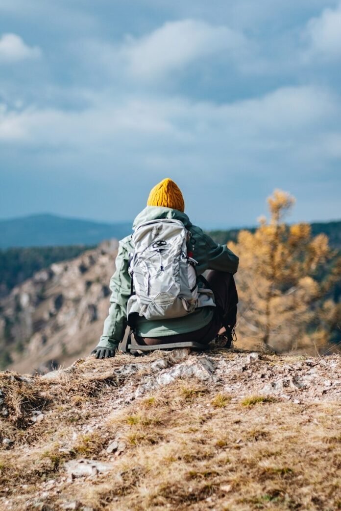 Photo by Dmitrii Shirnin A person sitting on top of a hill with a backpack